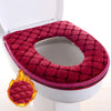 Una funda impermeable de asiento de inodoro de color rojo intenso y suave colocada sobre una taza de inodoro blanca.
