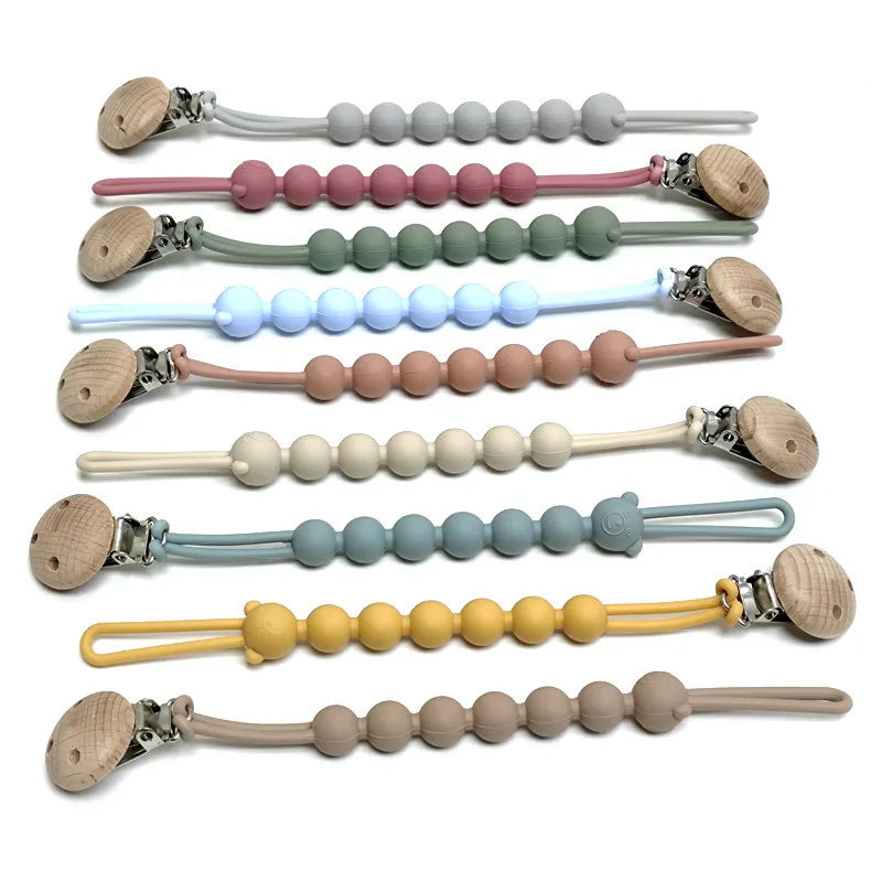 A collection of food-grade silicone pacifier clips with anti-lost chains in various pastel colors and natural wood tones.