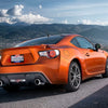 An orange Ford Mustang sports car with a Texas flag license plate parked on a scenic mountain road.
