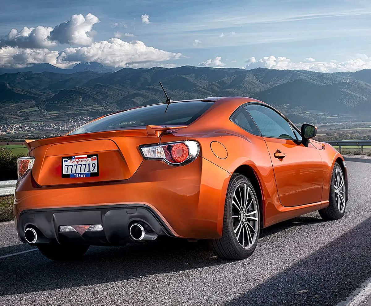 An orange Ford Mustang sports car with a Texas flag license plate parked on a scenic mountain road.
