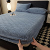 A blue textured mattress cover is shown on a bed, with a hand adjusting the elastic edge.