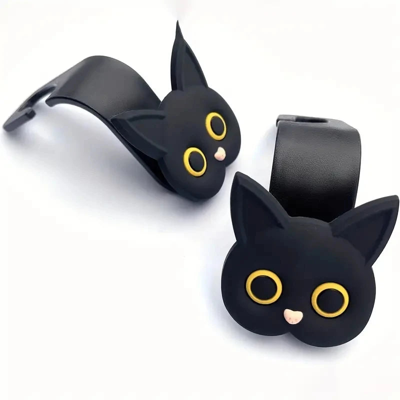 A set of two black 3D cat-shaped headrest hooks with gold eyes and pink noses.