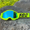 Neon yellow motocross goggles with blue mirrored lenses resting on a dark rock.