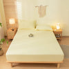 A light yellow fitted bed sheet set with pillowcases on a wooden bed frame in a bright room.