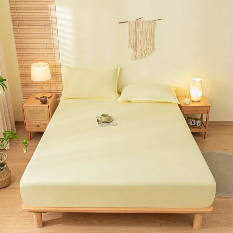 A light yellow fitted bed sheet set with pillowcases on a wooden bed frame in a bright room.