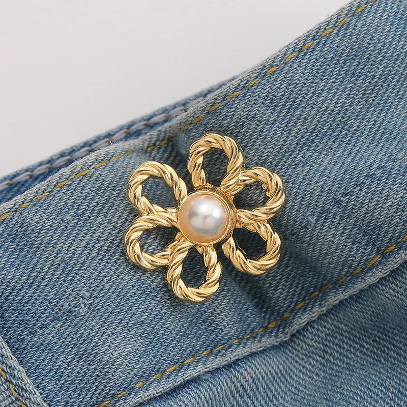 Gold-toned adjustable flower waist clip with a pearl center attached to a denim fabric.