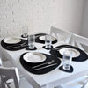 A white dining table set with black placemats, white plates, and clear glasses.