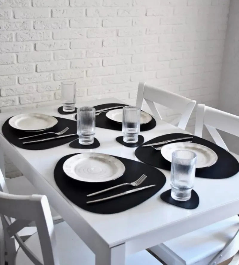 A white dining table set with black placemats, white plates, and clear glasses.