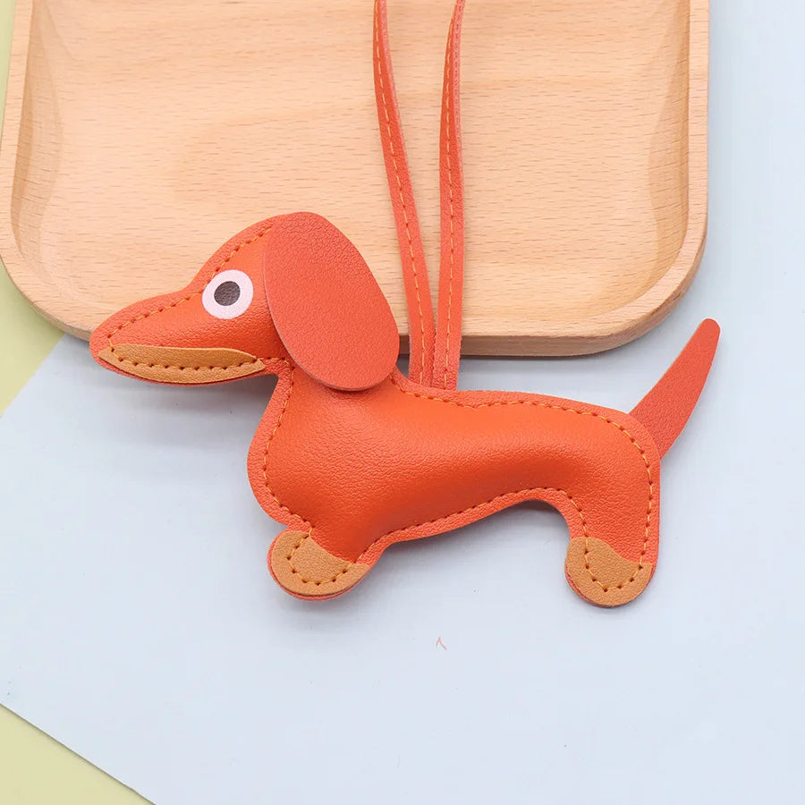 An orange dachshund shaped keychain made of PU leather with long ears and a loop for attachment.
