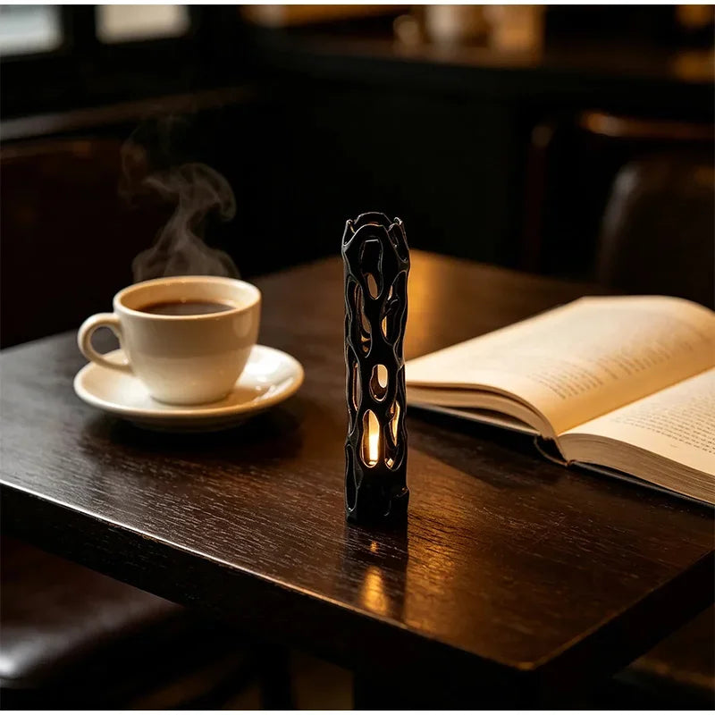 A black willow wood wishing stick stands next to an open book and a cup of coffee on a dark wooden table.