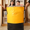 A bright yellow waterproof heavy-duty storage bag is displayed in front of a wooden shelf with clothing.