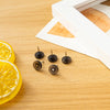 A collection of transparent push pins and thumb tacks are displayed on a wooden surface next to a lemon slice.