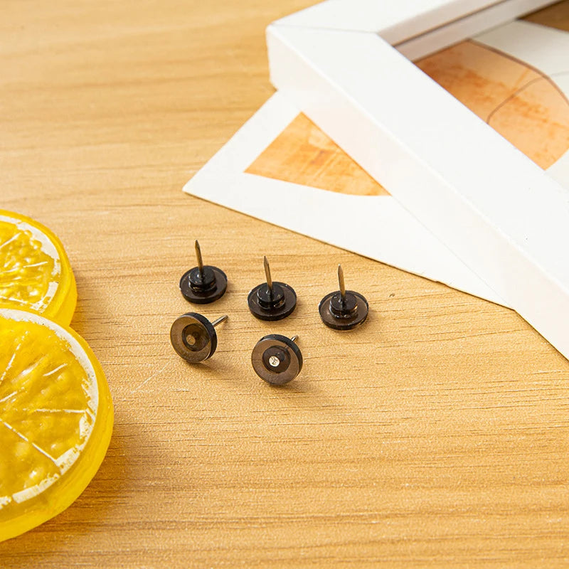 A collection of transparent push pins and thumb tacks are displayed on a wooden surface next to a lemon slice.