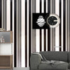 A close-up of black and white striped wallpaper featuring a round clock and a gray sofa.
