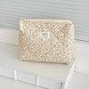A beige floral quilted cosmetic bag with a light yellow drawstring and a tag resting on a white surface.