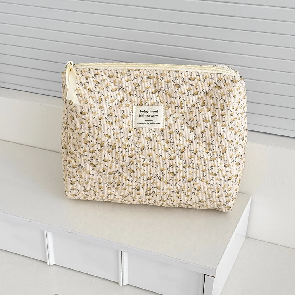 A beige floral quilted cosmetic bag with a light yellow drawstring and a tag resting on a white surface.