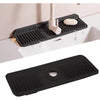 A black silicone faucet splash mat is installed in a white sink, featuring a drain and a small soap dish.