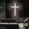 A white neon cross sign is mounted on a brick wall above a modern sofa.