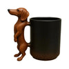 A brown dachshund figurine shaped like a puppy handle resting on a black coffee mug.