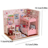 A pink wooden dollhouse miniature building kit featuring a bed, furniture, and decorative elements.