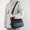 A man wearing a light gray jacket holds a black nylon crossbody sling bag.
