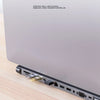 A silver USB-C docking station with multiple ports is shown lying on a wooden surface.
