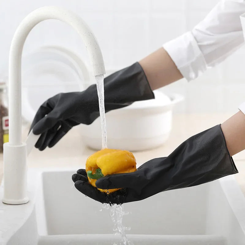 A hand wearing a black rubber cleaning glove is dripping water from a yellow fruit into a white sink.