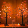 An LED Halloween birch tree with orange and purple lights stands next to a skeleton figure.