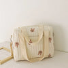 A cream-colored embroidered cotton diaper bag featuring bear and floral designs.
