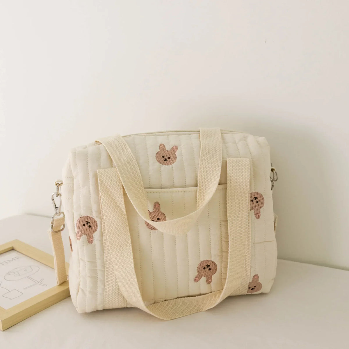 A cream-colored embroidered cotton diaper bag featuring bear and floral designs.