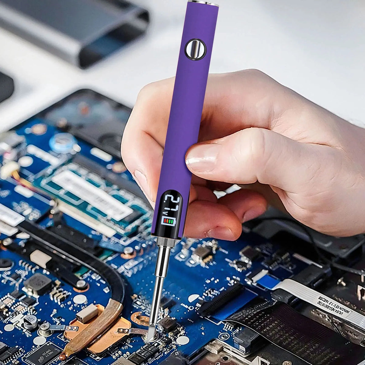 A hand holds a purple cordless USB-C soldering iron with a digital display tip over a blue circuit board.
