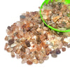 A pile of natural tumbled crystal stone chips in various shades of amber, brown, and clear quartz on a white background.