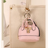 Pink compact PU leather earbud case with a gold keychain attached to a beige leather bag.