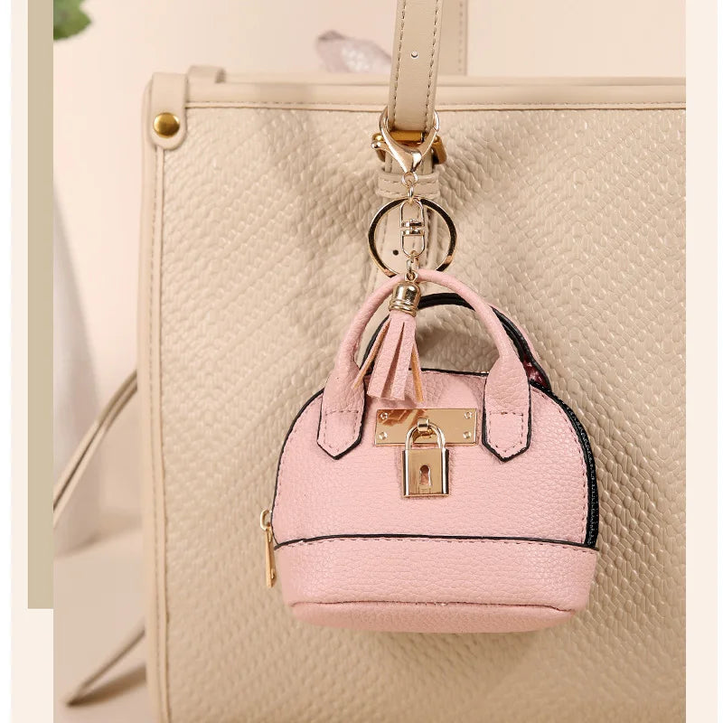 Pink compact PU leather earbud case with a gold keychain attached to a beige leather bag.