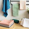 A set of four light colored waffle weave towels in shades of pink, beige, and green are displayed on a wooden surface.