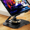 A hand holds a 360° rotating carbon steel tablet stand with a display on a wooden desk.
