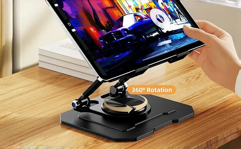 A hand holds a 360° rotating carbon steel tablet stand with a display on a wooden desk.