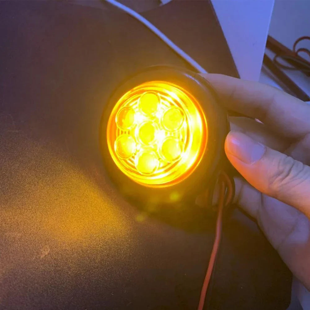 A hand is holding a round 7-LED flush mount tail light, illuminating the bright yellow lens.