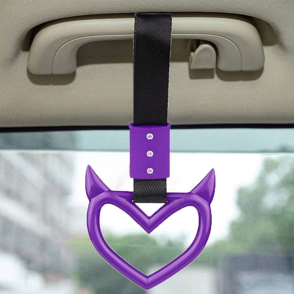 Purple heart-shaped ring drift handle with a black strap hanging from a car interior component.