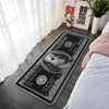 A black banknote pattern anti-slip soft floor mat placed on a light gray floor next to a bed.