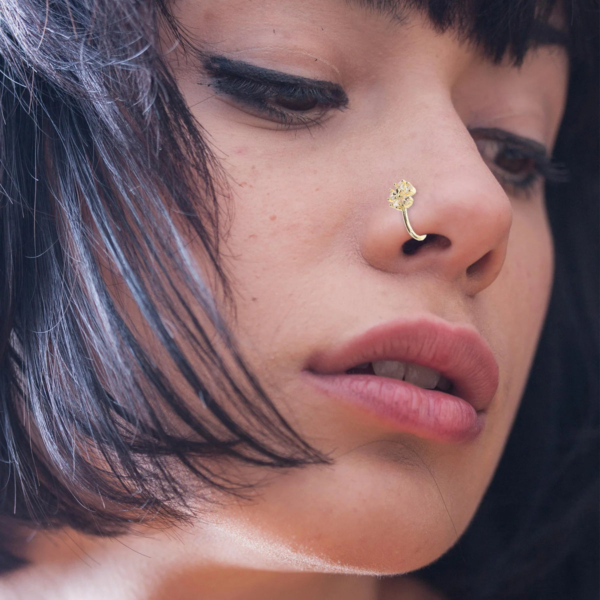 Close-up portrait of a woman wearing a gold nose cuff piercing on her nostril.