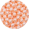 A close-up view of small, round, pinkish-orange imitation pearl beads for jewelry making.