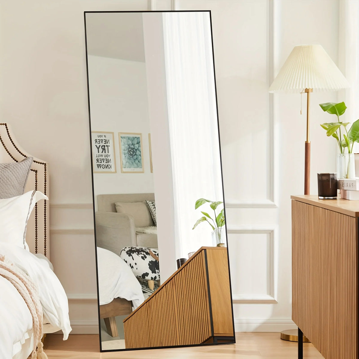 A full-length arched floor mirror with an aluminum frame reflecting a bright interior room.