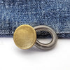 A round gold extender button attached to a silver spring ring, resting on a blue denim fabric.