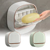 A hand is placing a yellow soap dish into the opening of a white wall-mounted ABS soap dish with a lid.