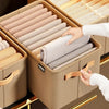 A hand is placing a rolled fabric item into a beige storage box filled with neatly folded fabric rolls.