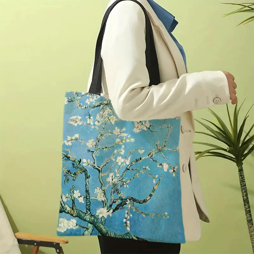 A person holds a light blue canvas tote bag featuring a white floral tree design against a pale green background.