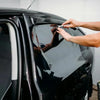 A person applies ceramic privacy tint film to a black car window.