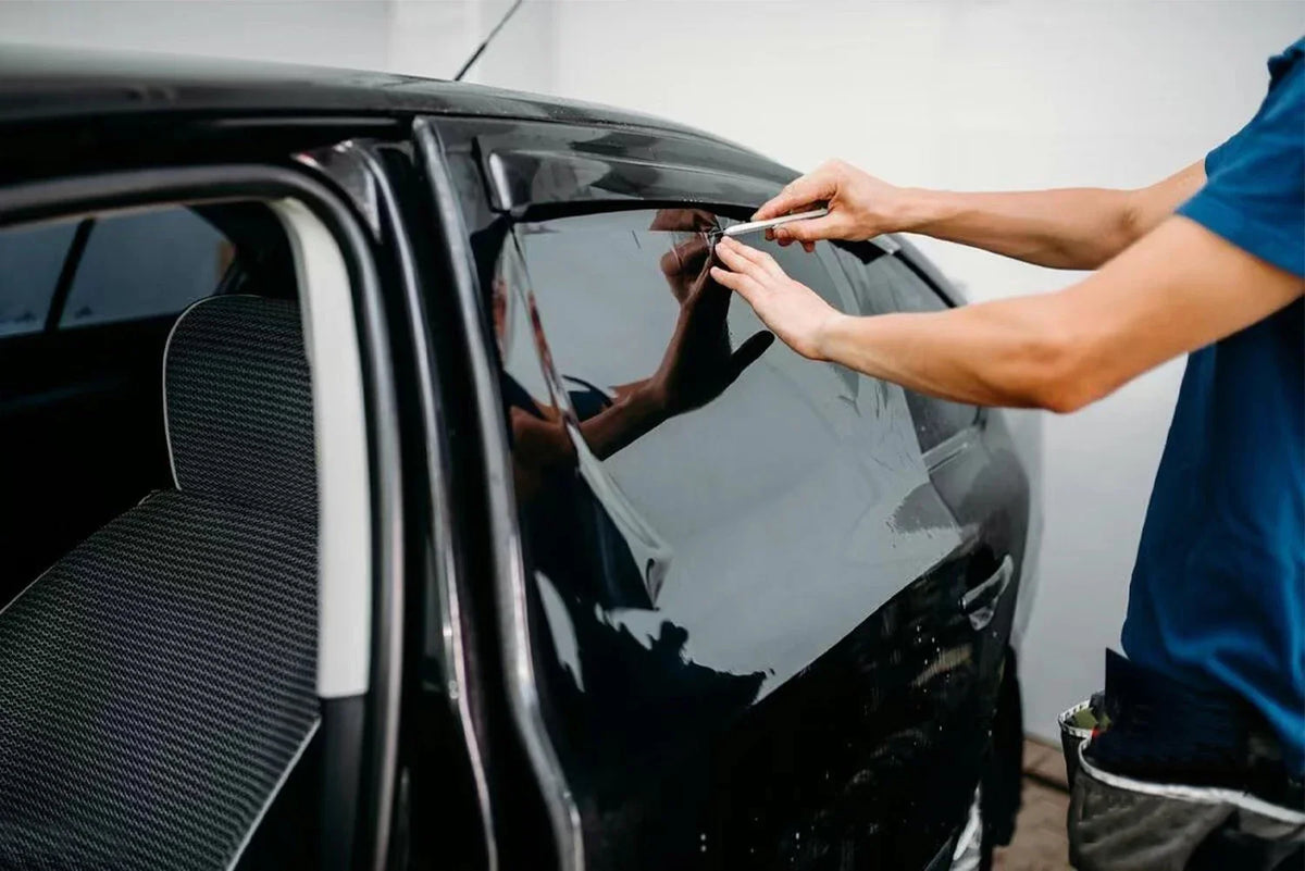 A person applies ceramic privacy tint film to a black car window.