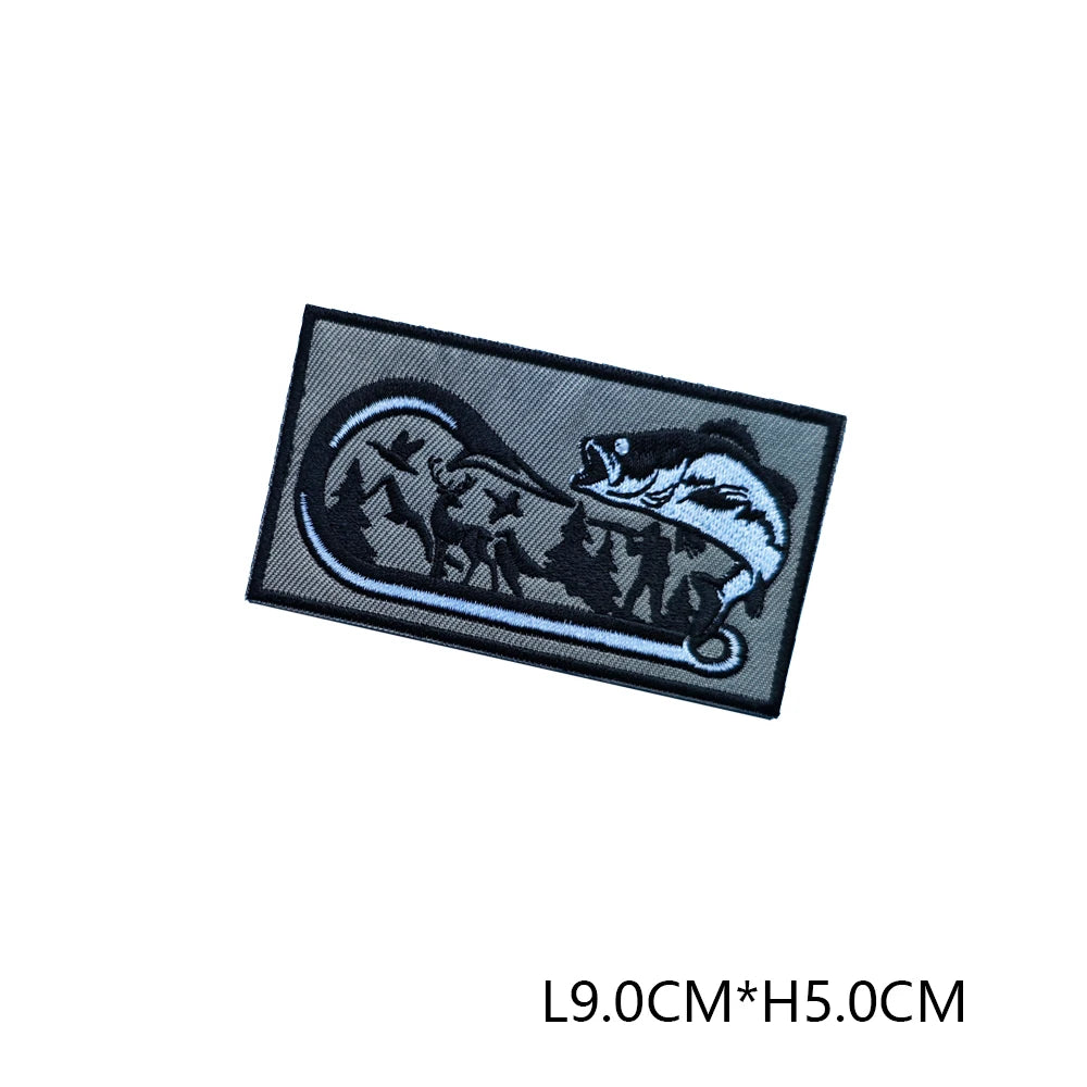 A black embroidered hunting patch featuring a silhouette of a fish and trees on a white background.